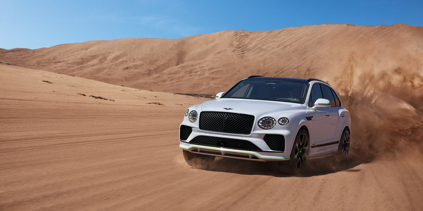 Bentley Leicester Bentley Bentayga Speed SUV front three quarter in Snow Quarts Pearlescent by Mulliner white paint driving dynamically through the desert