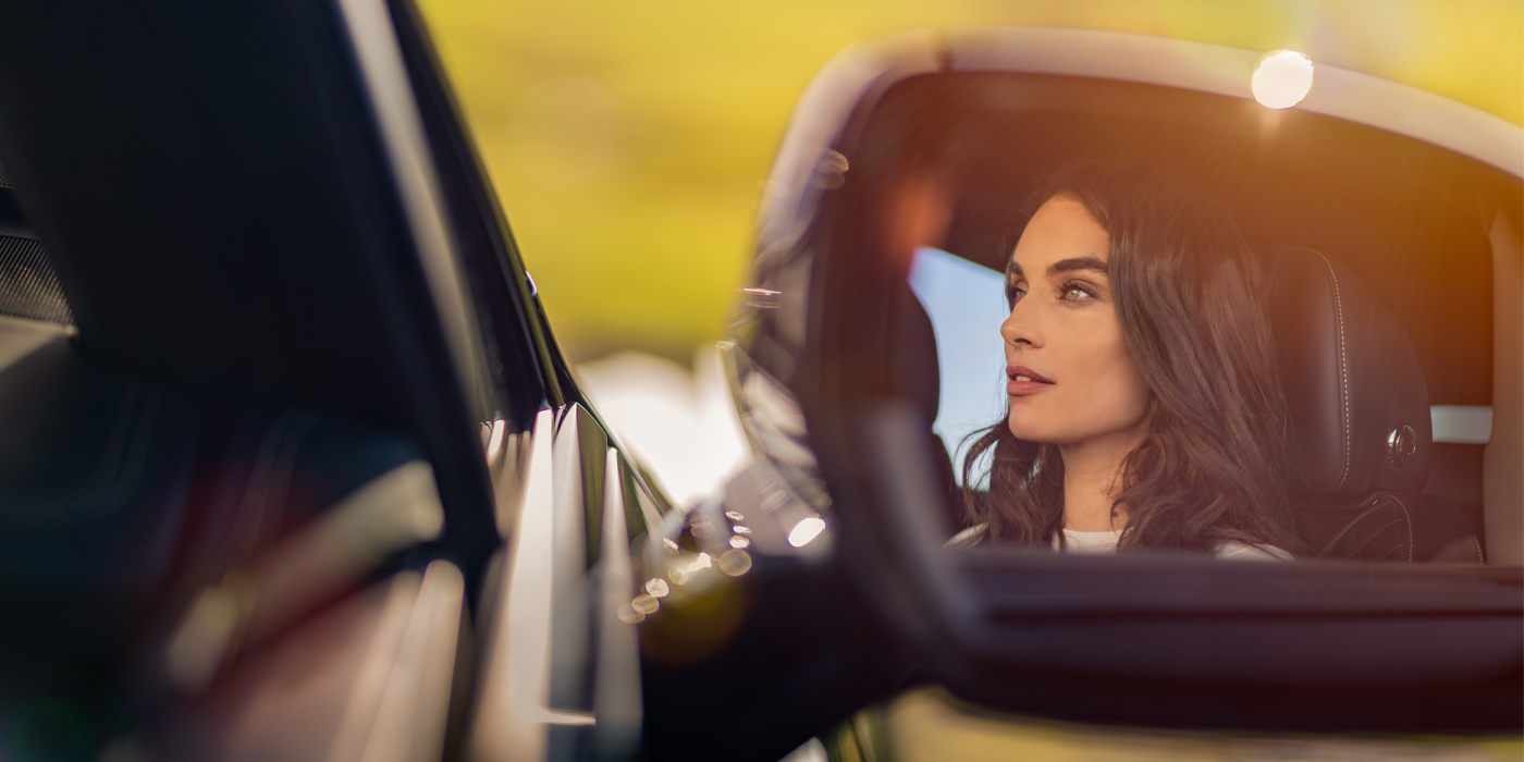 Bentley Leicester profile of dark haired woman's face in mirror of Bentley car in sunlight