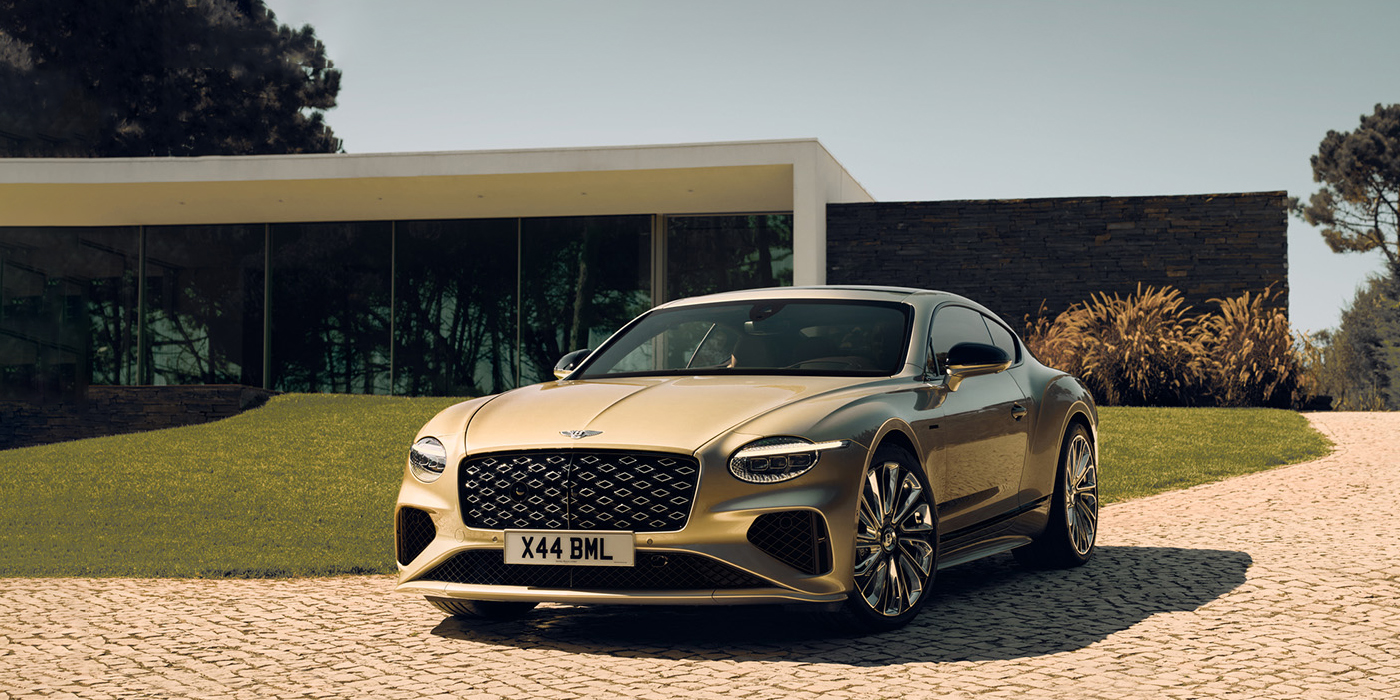 Bentley Leicester Bentley Continental GT Mulliner coupe front three quarters in Patina paint parked outside a glass fronted building with a grass lawn behind it