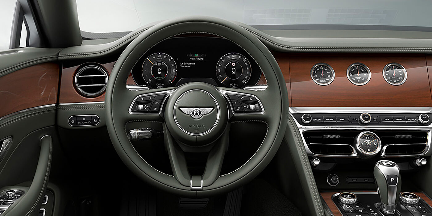 Bentley Leicester New Bentley Flying Spur sedan front cabin in Cumbrian Green hide and Crown Cut walnut veneer showing steering wheel and Rotating Display with three clocks on face