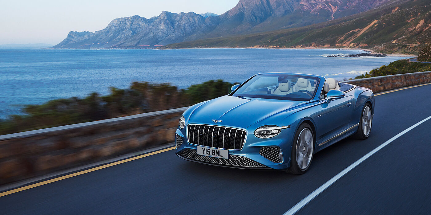 Bentley Leicester New Bentley Continental GTC Azure convertible in Light Windsor blue paint with 22 inch Azure wheels and chrome grill, driving dynamically by the sea