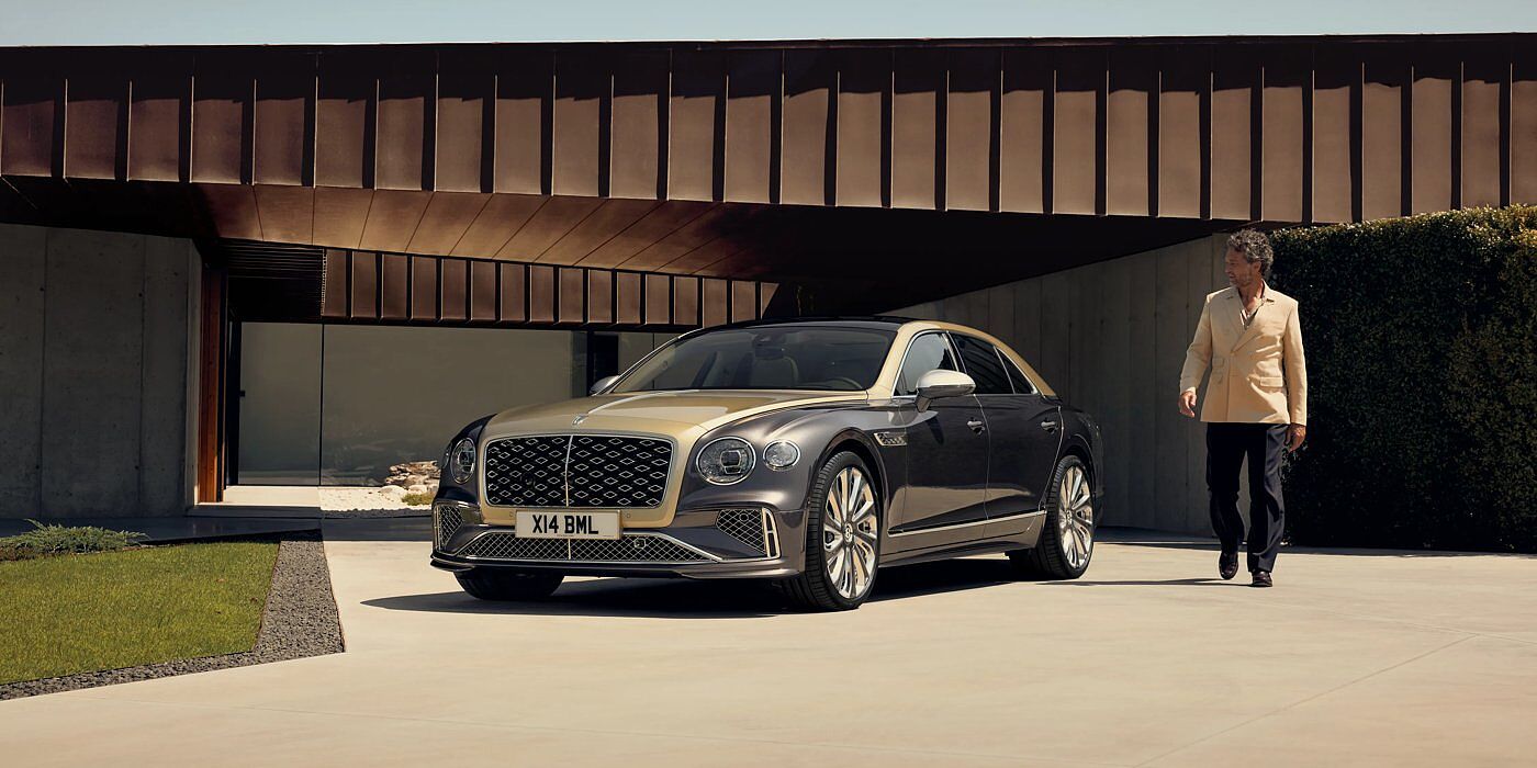 Bentley Leicester Bentley New Flying Spur Mulliner V8 hybrid sedan front three quarters in Rose Gold over Magnetic paint, parked near modern home