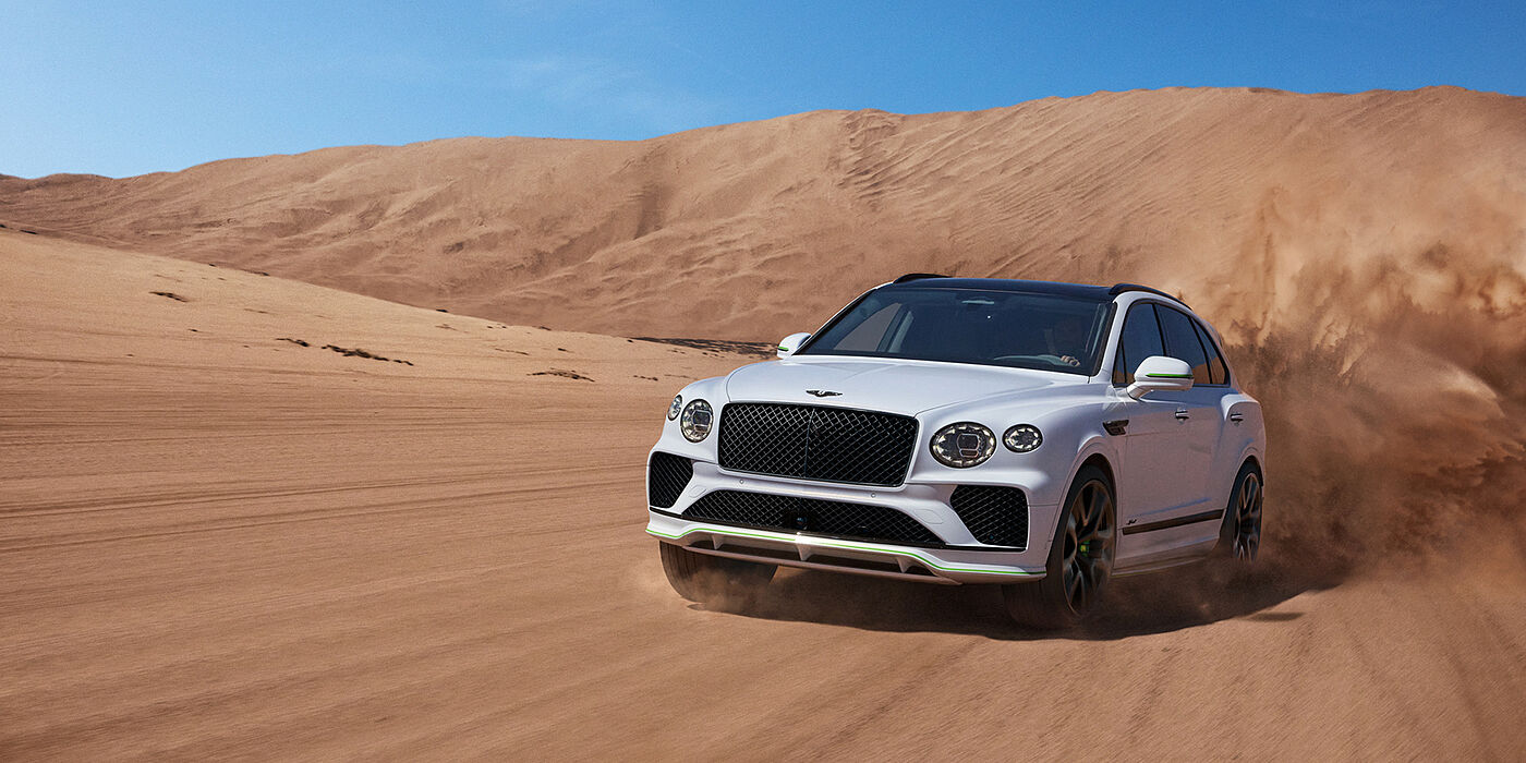 Bentley Leicester Bentley Bentayga Speed SUV front three quarter in Snow Quarts Pearlescent by Mulliner white paint driving dynamically through the desert