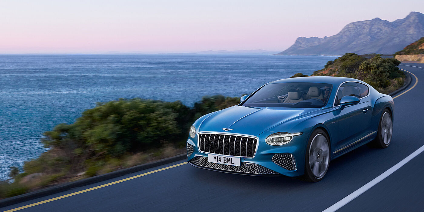 Bentley Leicester New Bentley Continental GT Azure coupe in Light Windsor blue paint with 22 inch Azure wheels and chrome grill, driving dynamically by the sea