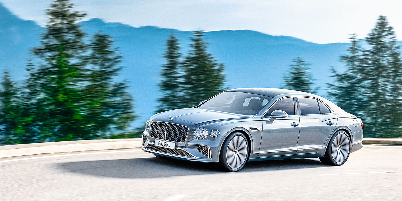 Bentley Leicester New Bentley Flying Spur sedan side view in Silverlake paint with ten spoke wheels and chrome matrix grille driving dynamically on a mountain road