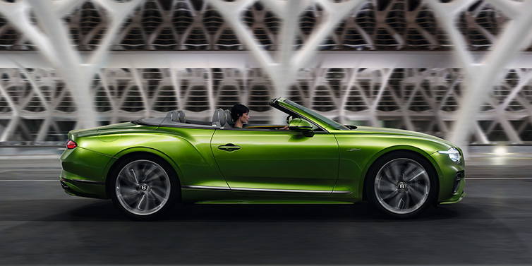 Bentley Leicester Bentley Continental GTC Speed convertible side profile in Tourmaline Green paint driving dynamically on a bridge at night