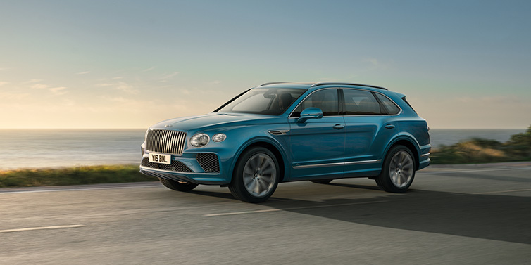 Bentley Leicester Bentley Bentayga Azure SUV in Topaz blue paint driving dynamically by the ocean with 22 inch 10 spoke directional wheels