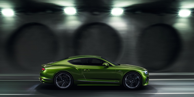 Bentley Leicester Bentley Continental GT Speed coupe profile in Tourmaline Green driving dynamically past a concrete wall at night