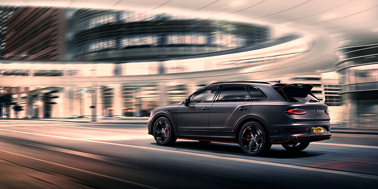 Bentley Leicester Bentley Bentayga S Black Edition SUV rear three quarter in Anthracite Satin paint driving dynamically through a city at night