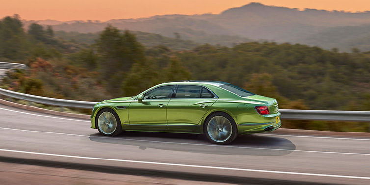 Bentley Leicester Bentley Flying Spur Speed sedan side profile in Tourmaline Green paint driving dynamically on a mountain road at sunset