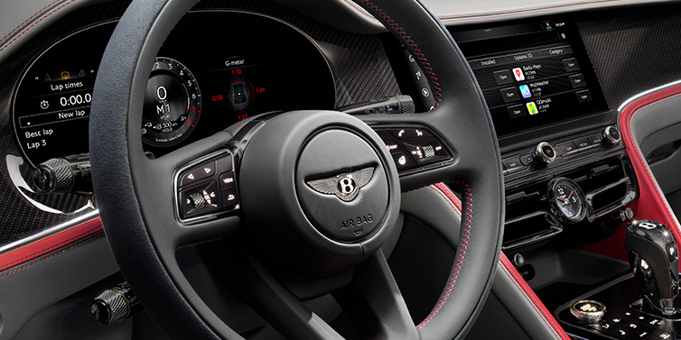 Bentley Leicester Bentley Flying Spur Speed sedan front interior detail showing steering wheel and driver screens surrounded with Hotspur red and Gravity Grey hides